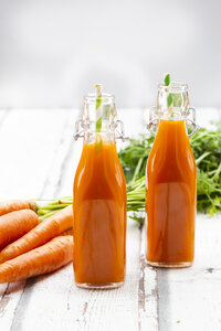 Karotten, Gläser mit Karottensaft und Bügelverschlussflaschen auf Holz - LVF07660