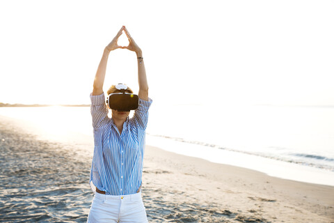 Blonde Frau macht eine Art von Yoga-Übungen an einem Strand in Thailand mit 3D-Virtual-Reality-Brille, lizenzfreies Stockfoto