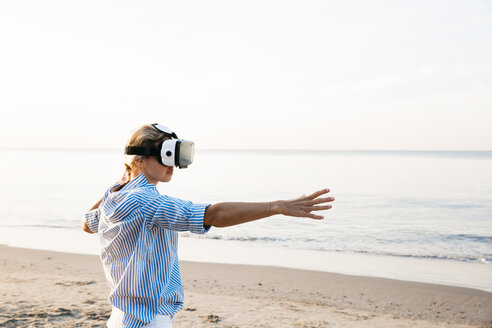 Blonde Frau macht eine Art von Yoga-Übungen an einem Strand in Thailand mit 3D-Virtual-Reality-Brille - HMEF00179