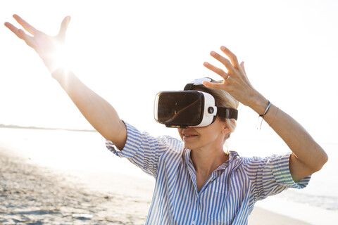Blonde woman doing kind of yoga exercises on a beach in thailand with 3D virtual reality goggles stock photo