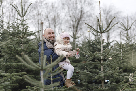 Vater und Tochter schmücken den Weihnachtsbaum auf einer Plantage, lizenzfreies Stockfoto