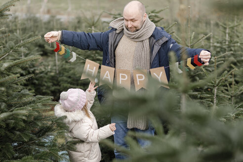 Vater mit Tochter hält Dekoration auf einer Weihnachtsbaumplantage - KMKF00736