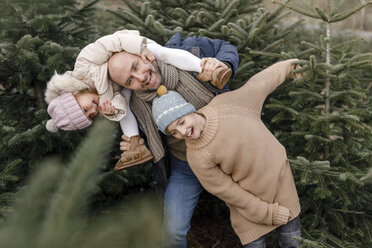 Porträt eines glücklichen Vaters mit zwei Kindern auf einer Weihnachtsbaumplantage - KMKF00744