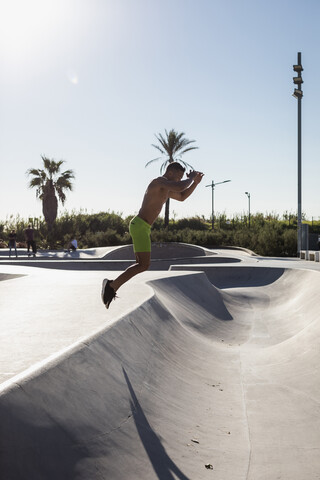 Muskulöser Mann mit nacktem Oberkörper springt in einem Skatepark, lizenzfreies Stockfoto