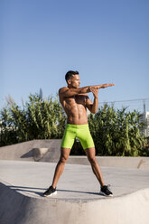 Muskulöser Mann mit nacktem Oberkörper bei Dehnungsübungen in einem Skatepark - MAUF02383