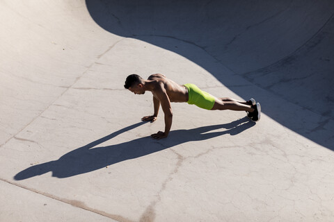 Muskulöser Mann mit nacktem Oberkörper macht Liegestütze in einem Skatepark, lizenzfreies Stockfoto