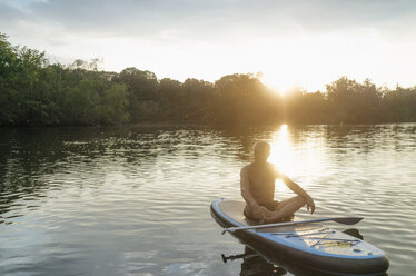 Älterer Mann sitzt bei Sonnenuntergang auf einem SUP-Board - GUSF01784