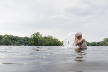 Älterer Mann in einem See, der sich Wasser ins Gesicht spritzt - GUSF01791