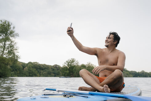 Mann sitzt auf einem SUP-Board auf einem See und macht ein Selfie - GUSF01799