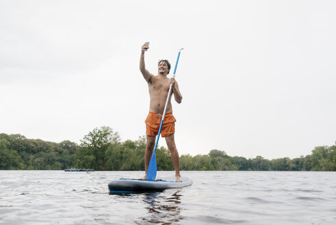 Mann steht auf einem SUP-Board auf einem See und macht ein Selfie - GUSF01800