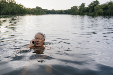 Senior man talking on cell phone in a lake - GUSF01806