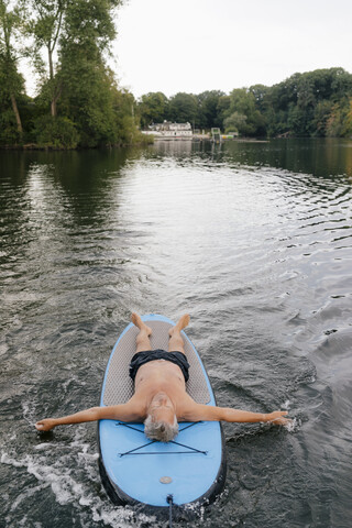 Älterer Mann auf SUP-Board auf einem See liegend, lizenzfreies Stockfoto