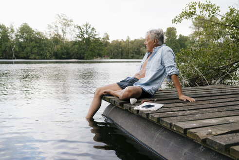 Älterer Mann sitzt auf einem Steg an einem See - GUSF01811
