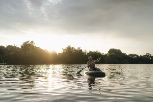 Älterer Mann auf SUP-Board bei Sonnenuntergang - GUSF01814