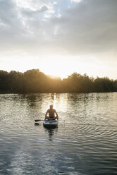 Älterer Mann sitzt bei Sonnenuntergang auf einem SUP-Board - GUSF01815