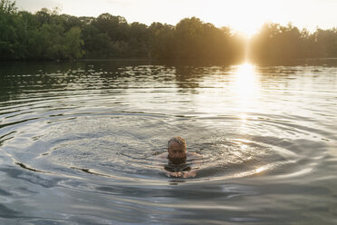 Älterer Mann schwimmt in einem See bei Sonnenuntergang - GUSF01818