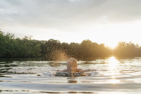 Älterer Mann schwimmt in einem See bei Sonnenuntergang - GUSF01819