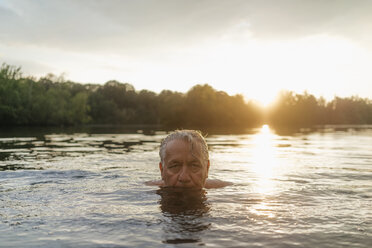 Älterer Mann schwimmt in einem See bei Sonnenuntergang - GUSF01821
