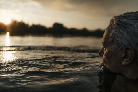 Älterer Mann schwimmt in einem See bei Sonnenuntergang, lizenzfreies Stockfoto