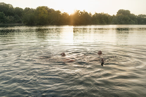 Alter und junger Mann schwimmen in einem See bei Sonnenuntergang - GUSF01824