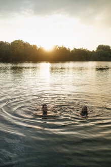 Alter und junger Mann schwimmen in einem See bei Sonnenuntergang - GUSF01825