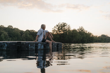 Älterer Mann sitzt auf einem Floß in einem See bei Sonnenuntergang - GUSF01830