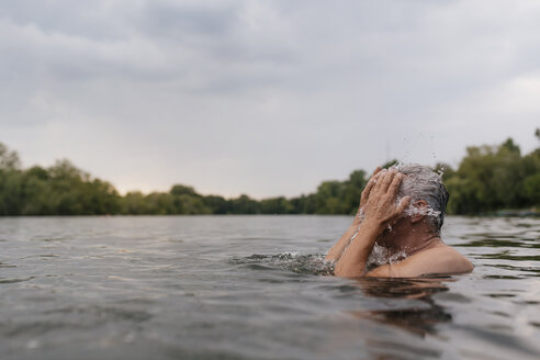 Älterer Mann in einem See, der sich Wasser ins Gesicht spritzt - GUSF01835