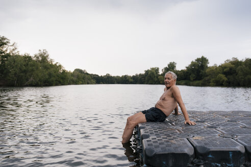 Senior man sitting on raft in a lake - GUSF01837