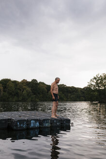 Älterer Mann steht auf einem Floß in einem See - GUSF01838