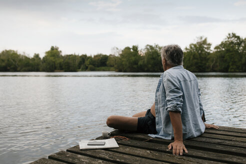 Älterer Mann sitzt auf einem Steg an einem See - GUSF01839