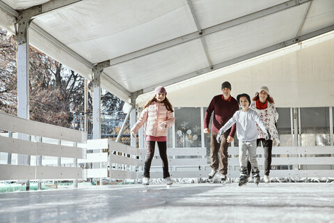 Familie mit zwei Kindern beim Schlittschuhlaufen auf der Eislaufbahn, lizenzfreies Stockfoto