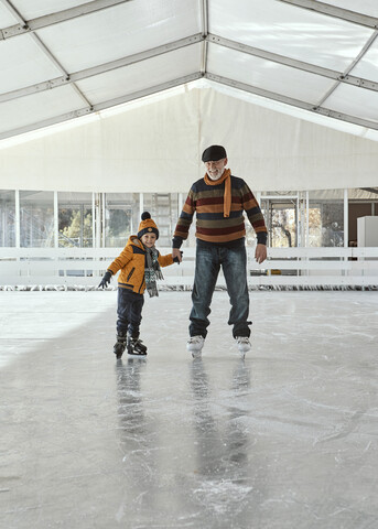 Großvater und Enkel auf der Eisbahn, Schlittschuhlaufen, lizenzfreies Stockfoto