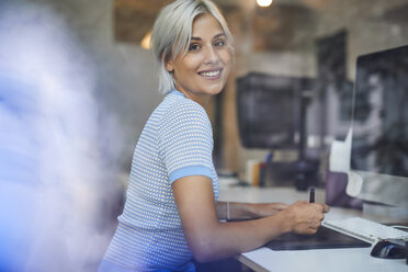 Young woman working in office, sitting at desk, smiling - PNEF01132