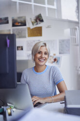 Junge Frau arbeitet im Büro, sitzt am Schreibtisch, lächelt - PNEF01136