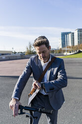 Mature businessman commuting in the city with his kick scooter, checking the time - GIOF05557