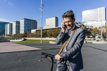 Älterer Geschäftsmann, der mit seinem Tretroller in der Stadt pendelt und sein Smartphone benutzt - GIOF05558