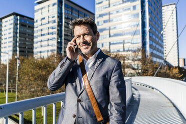 Businessman walking on a bridge, talking on the phone - GIOF05565