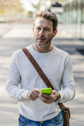 Mature man commuiting in the city, holding smartphone - GIOF05578