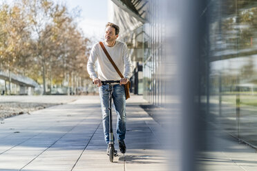 Mature man commuting in the city, using kick scooter on the pavement - GIOF05581