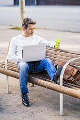 casual businessman sitting on a bench, working relaxed in the city - GIOF05586