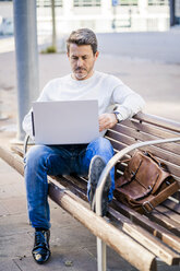 lässiger Geschäftsmann, der auf einer Bank sitzt und entspannt in der Stadt arbeitet - GIOF05587