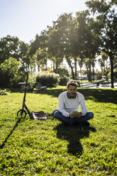 lässiger Geschäftsmann, der im Gras in einem Park sitzt und ein Smartphone und Kopfhörer benutzt - GIOF05606