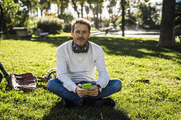 lässiger Geschäftsmann, der in einem Park im Gras sitzt und sein Smartphone benutzt - GIOF05607