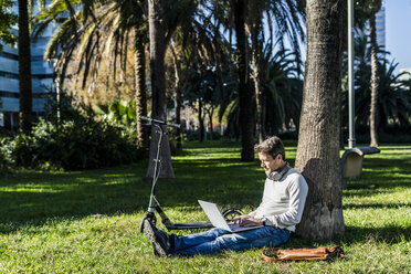 casual businessman sitting on grass in a park, using laptop - GIOF05610