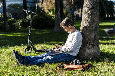 casual businessman sitting on grass in a park, using laptop - GIOF05611