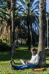 lässiger Geschäftsmann sitzt im Gras in einem Park und benutzt einen Laptop - GIOF05612