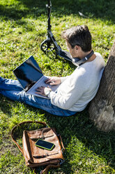 lässiger Geschäftsmann sitzt im Gras in einem Park und benutzt einen Laptop - GIOF05613