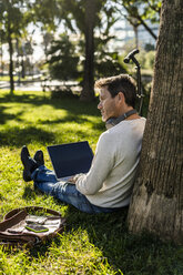 casual businessman sitting on grass in a park, using laptop - GIOF05614