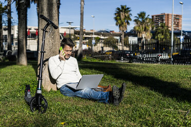 lässiger Geschäftsmann sitzt im Gras in einem Park und benutzt einen Laptop - GIOF05615