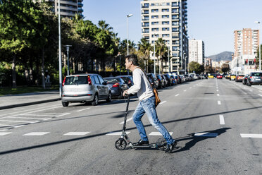 Mature man commuiting in the city with his kick scooter, crossing a street - GIOF05619